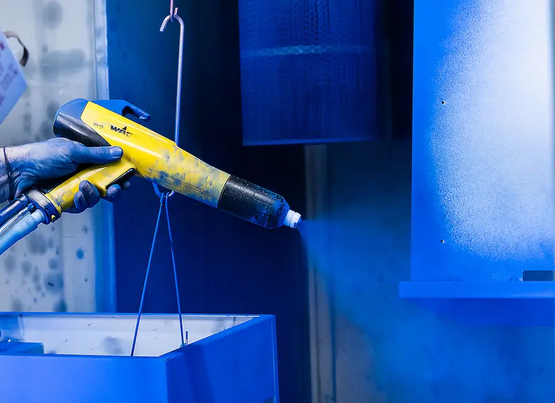 Powder gun laying blue powder coat onto a hanging part