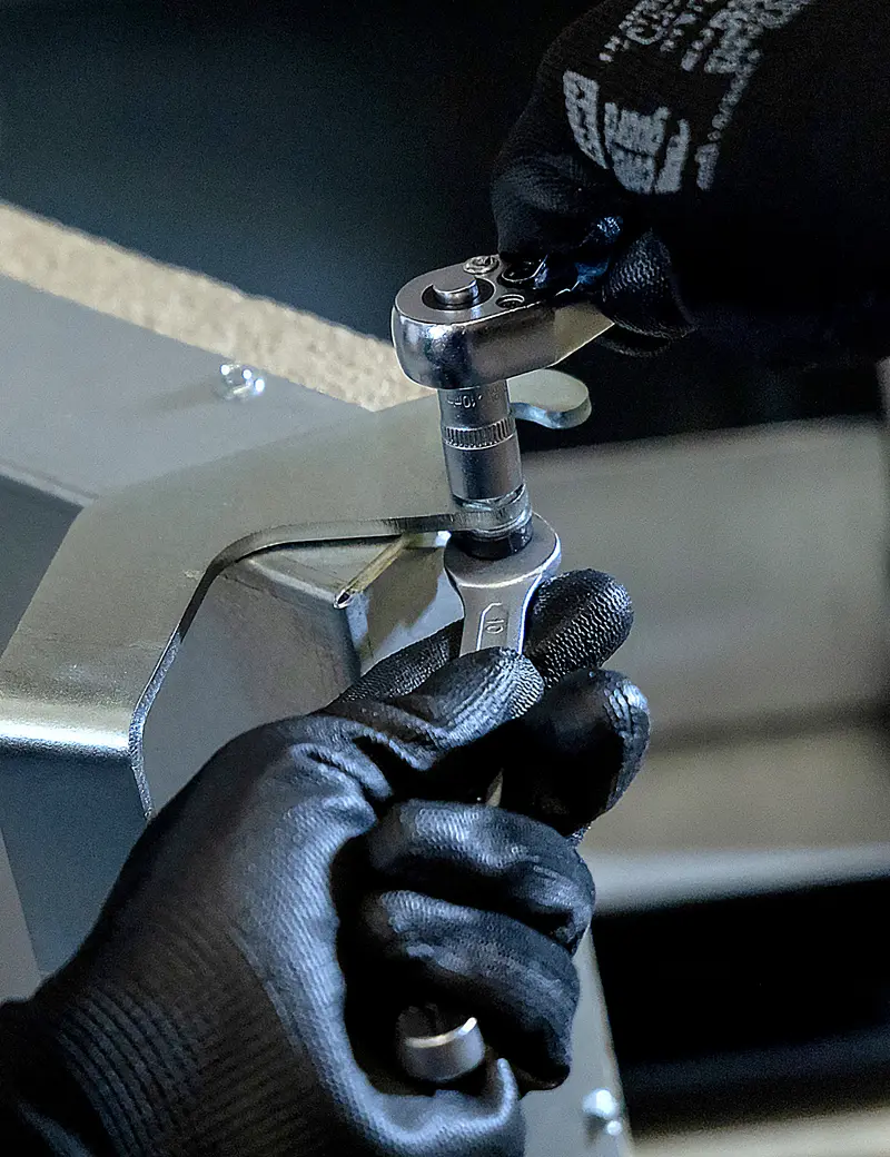 Assembly close-up: gloved hands working a ratchet on a bracket fastening